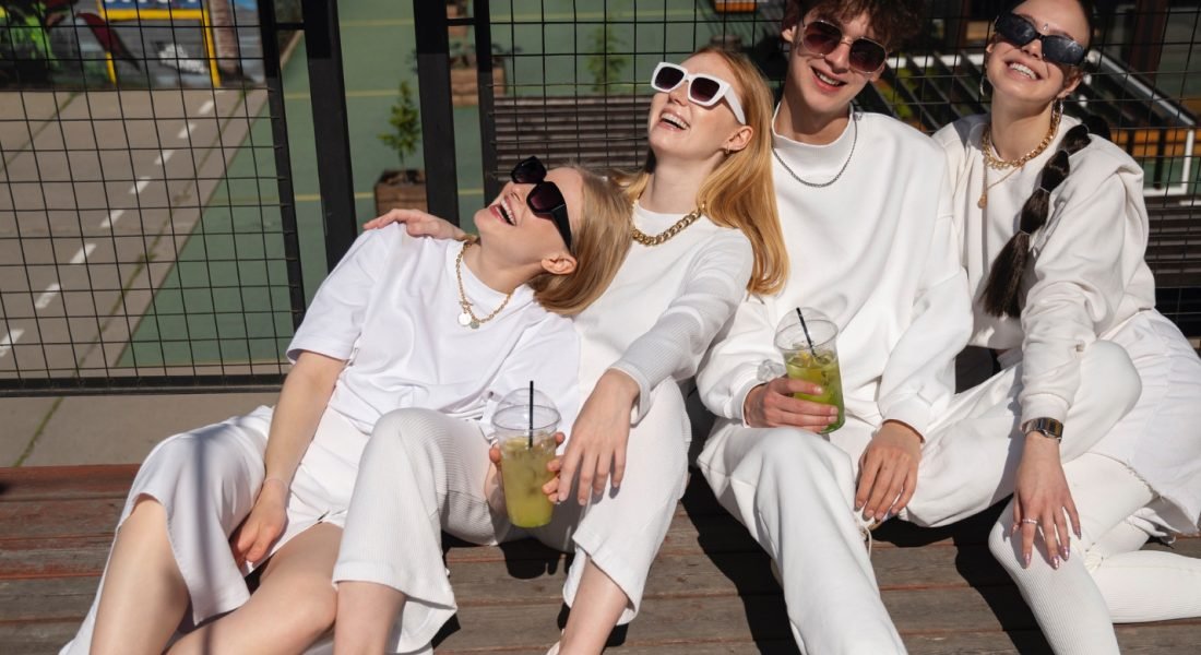 Group of four friends in stylish white outfits enjoying drinks, embodying a relaxed and luxurious lifestyle, reflecting the essence of Maison Alhambra's commitment to accessible luxury and timeless elegance.